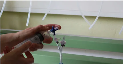 Hands hold a syringe and a glass with a tube to fill the gas from the syringe into the glass