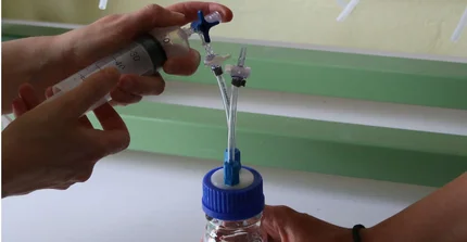Hands hold a syringe and a glass with a tube to fill the gas from the syringe into the glass