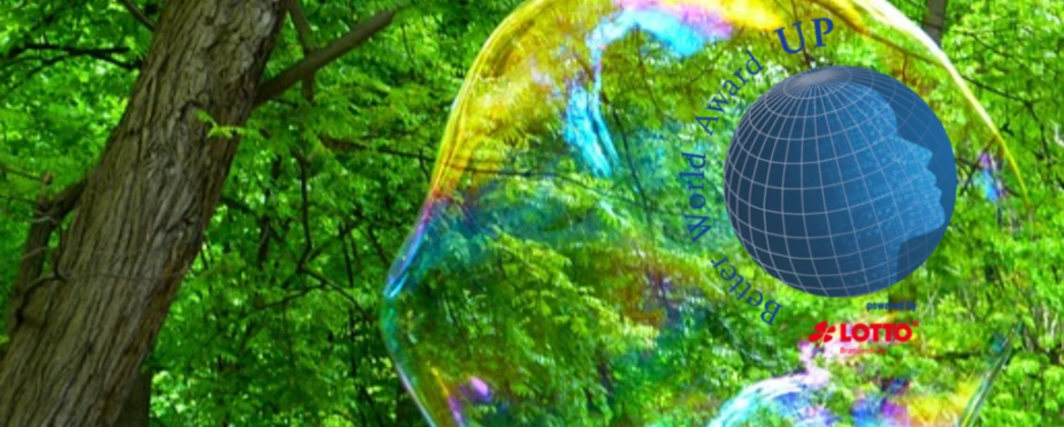 Ein Globus umgeben mit Schrift "Better World Award" und "powered by Lotto Brandenburg". Im Bildhintergrund das grüne Laubdach eines Waldes und große Seifenblasen. - 
