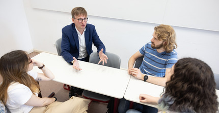 Professor Neitzel sitzt mir 3 Studierenden an einem Tisch und redet gestikulierend