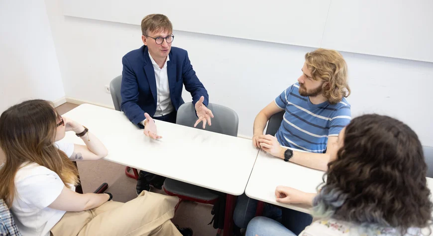 Professor Neitzel sitzt mir 3 Studierenden an einem Tisch und redet gestikulierend
