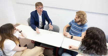 Professor Neitzel sitzt mir 3 Studierenden an einem Tisch und redet gestikulierend