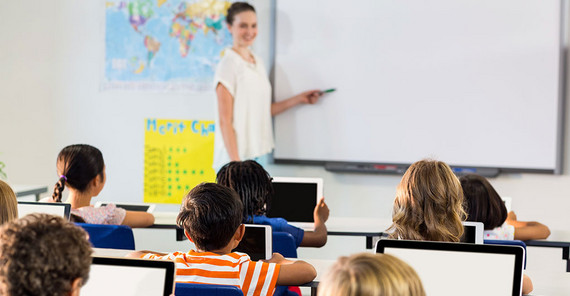 Eine Schulklasse mit Lehrerin die an der Tafel etwas zeigt.