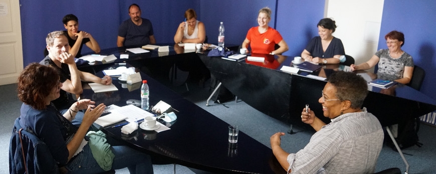 Teilnehmende der Language-Staff-Week an der Universität Masaryk sitzen im Kreis um einen Tisch und unterhalten sich.