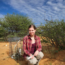NamTip researcher sitting in front of savanna shrubs with measuring devices, a book and a pen