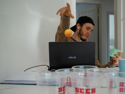 Mensch hinter Laptop der Ball in Becher auf Tisch wirft und dabei lernt