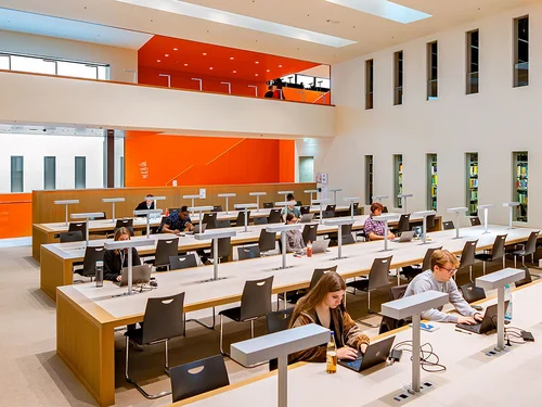 Ein großer Saal mit Tischen und Stühlen, mit einigen Personen, die an Laptops arbeiten
