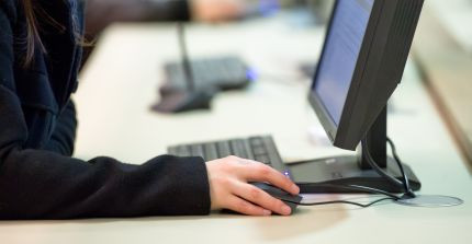 Es ist ein PC Arbeitsplatz abgebildet. es ist ein Bildschirm und der Arm eines Studierenden zu sehen.