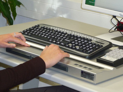 Zwei Hände schreiben auf einer Tastatur für Seh-Behinderte.