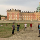 Zu sehen ein Gruppenbild des Jazzchors Campus Golm bei der Chorfahrt im Sommer 2021. Die XX Teilnehmer der Chorfahrt sitzen auf Holzbänken der Jugendherberge, die idyllisch im Wald gelegen ist.