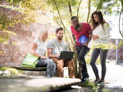 StudentInnen draußen schauen auf Notebook