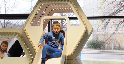 Kinder spielen auf einem Indoor-Spielplatz. Ein Junge sitzt auf der Rutsche.