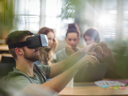 Ein Mann benutzt eine VR-Brille und wird dabei von drei anderen Personen beobachtet