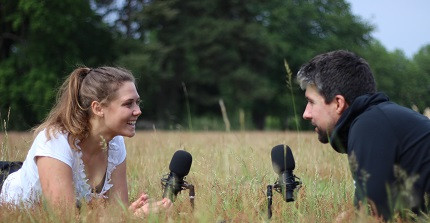 Zwei ehemalige Lehramtstudierende liegen auf der Wiese. Vor ihnen sind Mikrophone platziert.