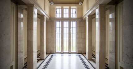 Großes, mehrstöckiges Foyer aus Marmor mit hohen Fenstern im Hintergrund