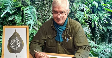 Mike Wessel an einem Tisch sitzend mit Scherenschnittarbeiten vor sich.