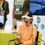 Ein Kind mit einer VR Brille sitzt auf einem Stuhl und hält einen Controller in der Hand
