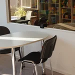 Blick in einen Therapieraum. Ein Tisch und zwei Stühle vor einer Spiegelscheibe.