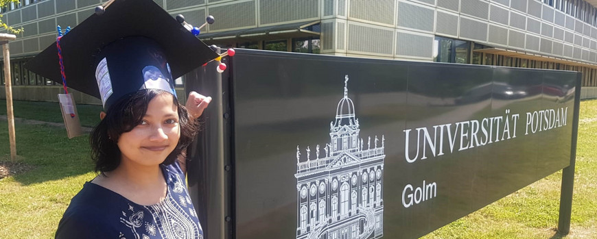 Noverra M. Nizardo is standing in front of a sign of the University of Potdsam in Golm.