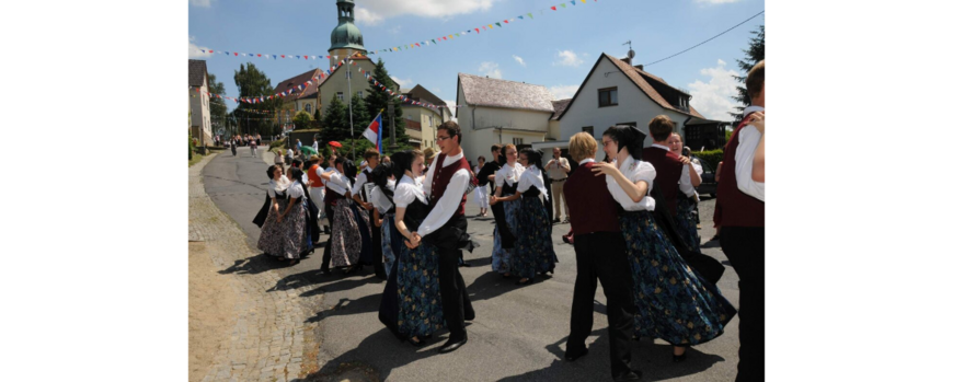 Tanzende Paare in Katholischer Tracht entlang einer Dorfstraße