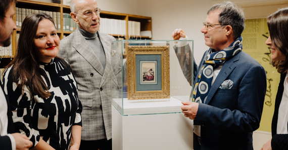 Fünf Menschen stehen um eine Vitrine betrachten das Gemälde darin