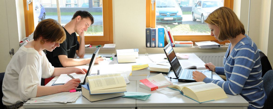 Drei Studierende sitzen sich in der Bibliothek an einem Tisch gegenüber