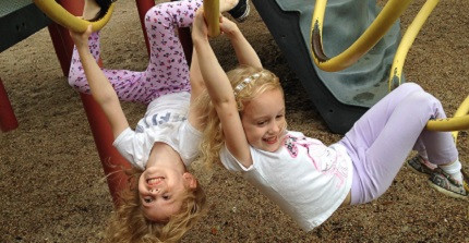 Zwei Kinder hängen kopfüber an Spielgeräten auf einem Spielplatz.