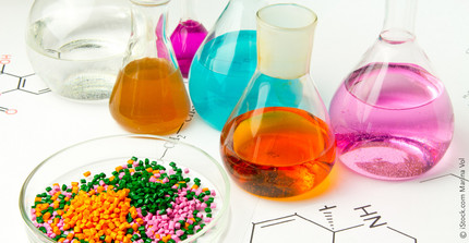 various Erlenmeyer and round bottom flasks with colored liquids and next to them a bowl with plastic granules