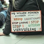 An activist sits on the floor with a sign describing the impact of aviation