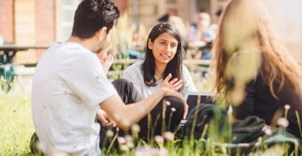 Three students sitting on the lawn on Am Neuen Palais campus talking to each other.