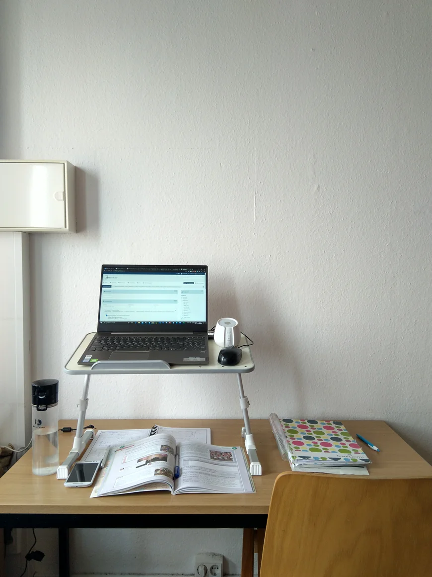 Laptop auf Laptopständer. Bücher und Wasserflasche daneben.