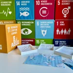 Ein Würfel zeigt das SDG 11 Nachhaltige Städte und Gemeinden, den Spielplan des GeoBreakouts, auf dem die Region abgebildet ist und die drei Küstenformen Flachküste, Steilküste und Delta.