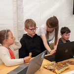 Zwei Erwachsene und drei Kinder arbeiten gemeinsam an Laptops.