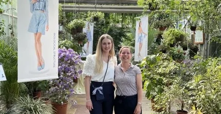 women standing in greenhouse between plants and exhibition posters