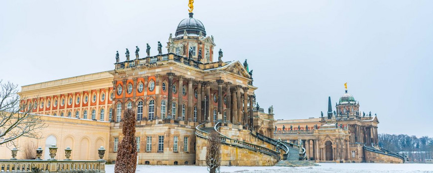 zwei historische Gebäude am Neuen Palais hinter verschneiten Wiesen