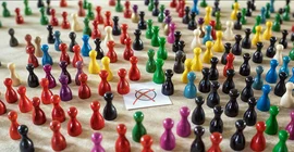 Spielfiguren in den Farben politischer Parteien um einen Mini-Stimmzettel versammelt.