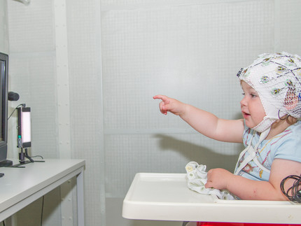 Kind mit EEG-Kappe auf dem Kopf zeigt auf einen Bildschirm