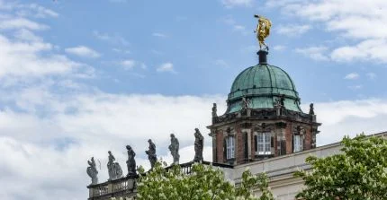 Dach des historischen Nordcommuns mit Figuren am Rand und auf der Kuppel, am unteren Rand blühende Kastanienbäume