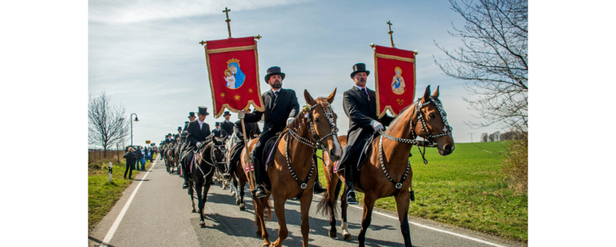 Eine Festzug entlang einer Landstraße aus berittenen Männer in schwarzer Tacht und roten Bannern