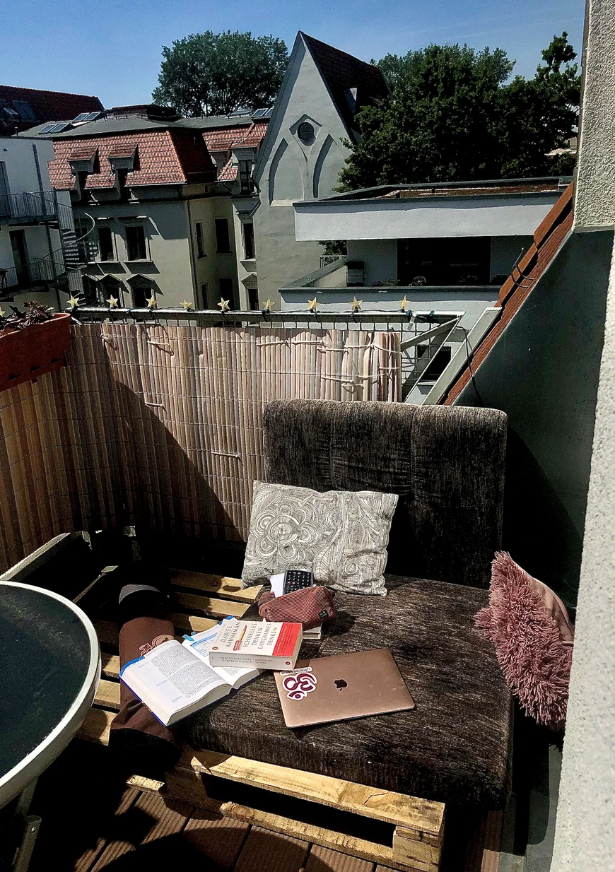 Sessel auf einem Balkon, darauf liegen geschlossener Laptio und Bücher und Kissen