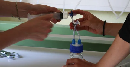 Hände halten eine Spritze und ein Glas mit Schlauch, um das Gas aus der Spritze in das Glas zu füllen