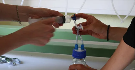 Hände halten eine Spritze und ein Glas mit Schlauch, um das Gas aus der Spritze in das Glas zu füllen