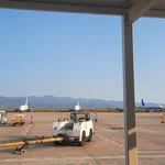 Flughafen von Castellón mit Flugzeugen und Flughafenfahrzeugen im Vorder- und Mittelgrund. Im Hintergrund Berge und darüber wolkenloser Himmel.