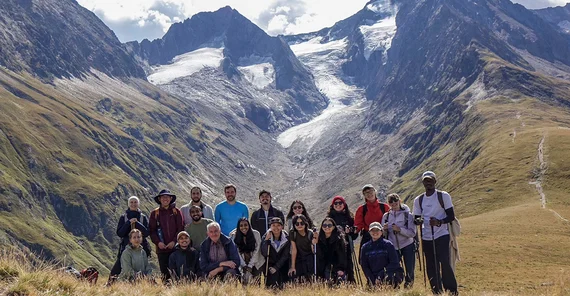 A group of people posing in front of impressive mountain side.