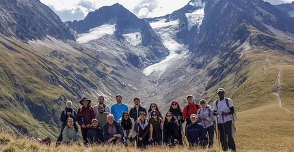 Eine Gruppe von Menschen posiert vor hohen Bergen im Hintergrund für ein Gruppenfoto