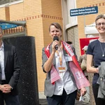 Drei Personen, die Person in der Mitte hält ein Mikrofon