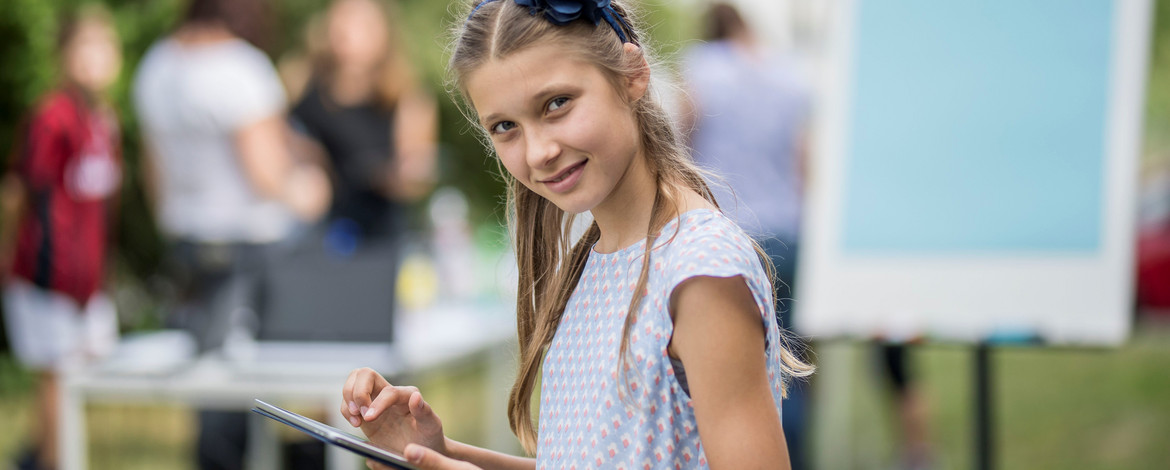 Mädchen lernt mit Hilfe von verschiedenen Medien im Schulgarten