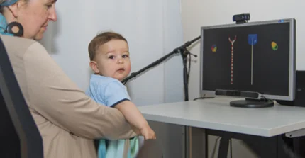 A child is sitting on their mothers lap and looking at a screen