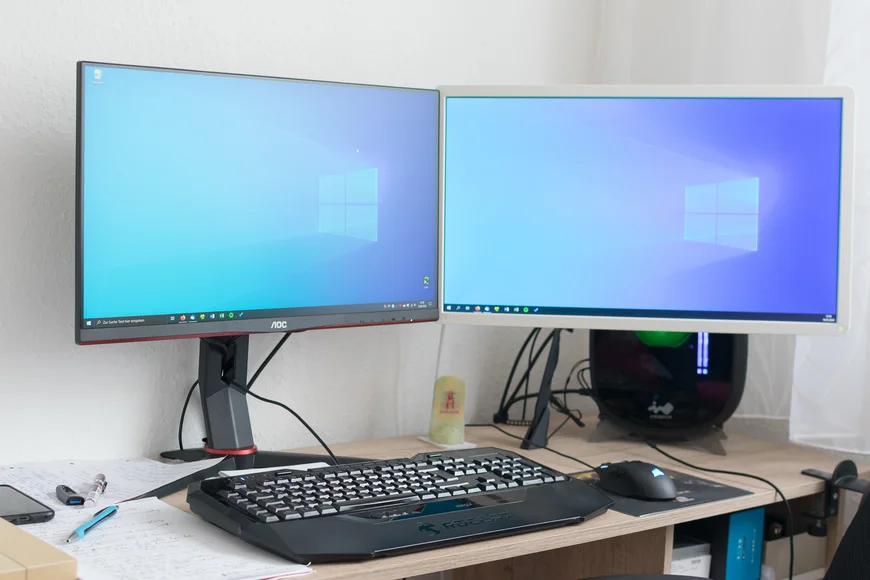 Schreibtisch mit 2 sehr großen Bildschirmen, großer Tastatur, Maus und Schreibzeug