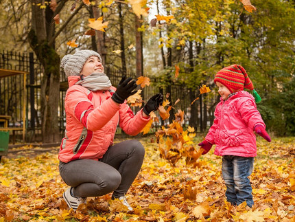 Eine Frau und ein Kind spielen im Herbstlaub. Die Frau wirft das Laub nach oben.